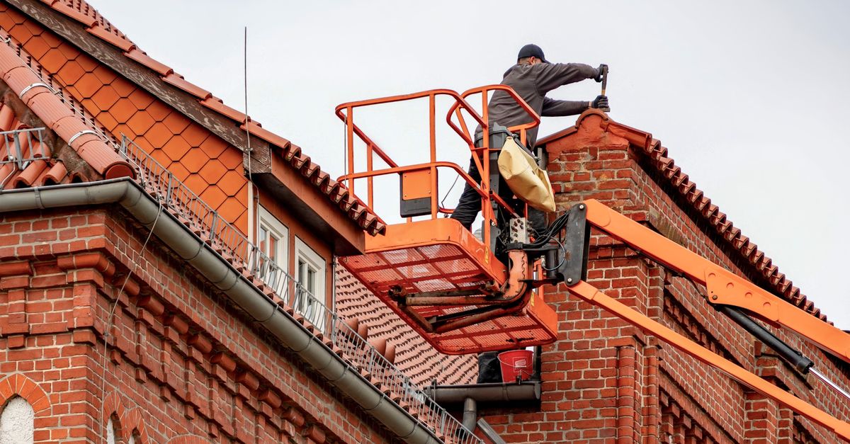 Couvreur intervenant sur une toiture en tuiles depuis une nacelle élévatrice